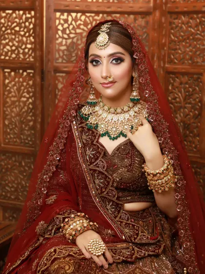 A regal bridal portrait. The makeup is pure glamour, with sharp, defined eyes and a perfectly contoured base to match her ornate maroon lehenga.