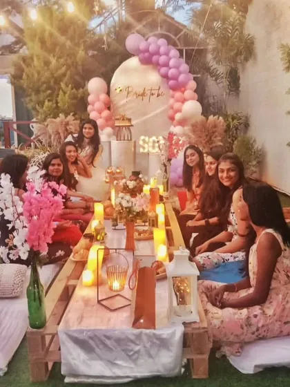 A lovely "Bride to be" celebration with a boho picnic theme. A group of friends gathers around a low wooden table decorated with candles and flowers, showing how perfect these setups are for small group events.