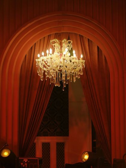 A crystal chandelier framed by an archway and heavy red drapes, creating a sense of theatrical grandeur.