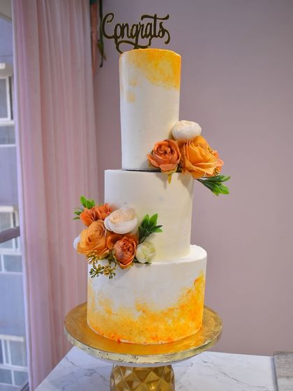 A closer view of the three-tier orange watercolor wedding cake, showcasing the vibrant yet soft blending of colors and the arrangement of fresh orange and white flowers.