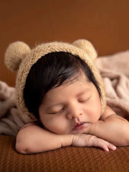 The tiny details are everything. This close-up highlights the soft cheeks, delicate lips, and peaceful expression of a sleeping newborn, complemented by a hand-knitted bear bonnet that adds a touch of cozy charm.