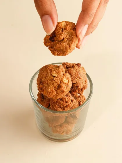 A hand delicately picking up a bite-sized cookie, emphasizing its small, snackable nature.