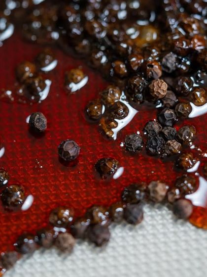A close-up of peppercorns suspended in a beautiful, amber-colored caramel, a component for an adventurous new chocolate recipe.