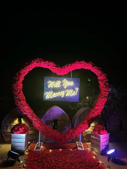 For a truly romantic gesture, we created this large heart-shaped arch from hundreds of red roses. At the center, a 'Will You Marry Me?' neon sign glows, creating a breathtaking focal point for an outdoor proposal.