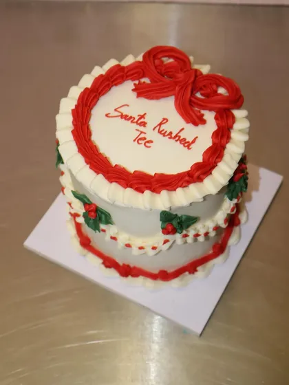 A classic Christmas-themed cake with red and white vintage piping, holly details, and a big red bow.