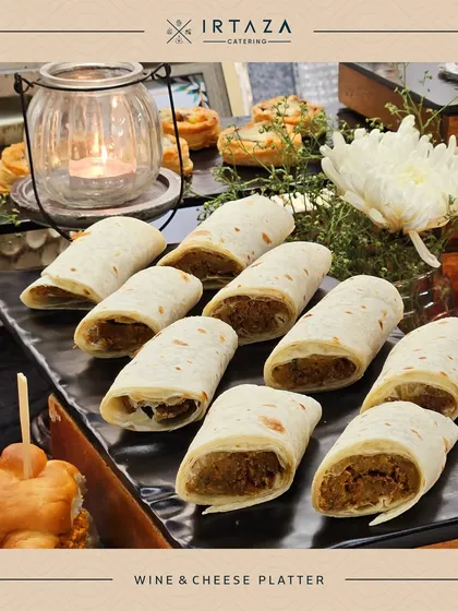 A platter of mini wraps, part of a wine and cheese spread. These bite-sized wraps are filled with savory goodness and are perfect for guests to enjoy with a glass of wine.