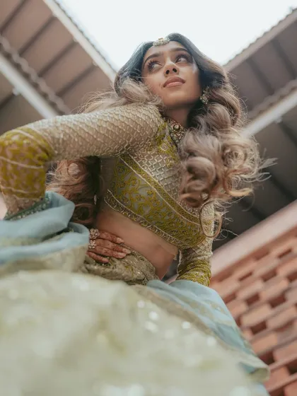 A creative, low-angle shot of the bride, emphasizing the beautiful flare of her lehenga and her confident pose during her Mehendi event.