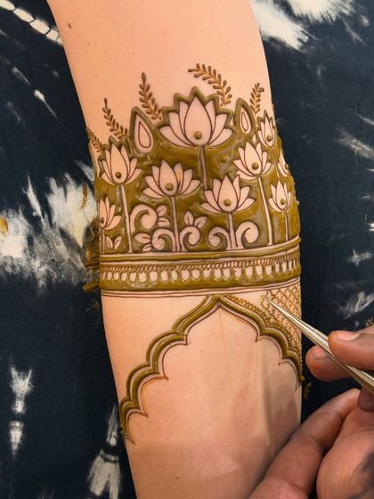 An action shot of me filling in a detailed lotus armband. You can see the fine tip of my henna cone, which allows for precise and intricate work.
