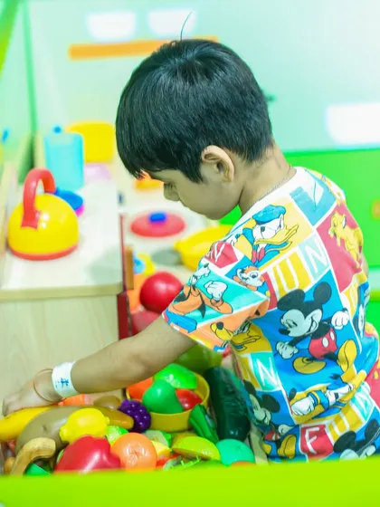 A young boy carefully arranges toy fruits and vegetables in our pretend play kitchen, a great activity for learning and imagination.