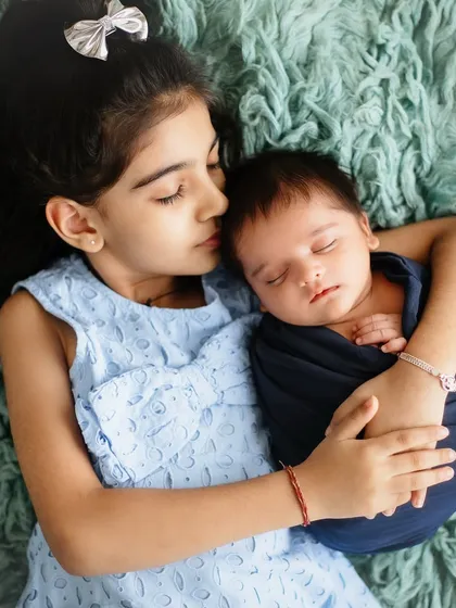 A tender moment between a sister and her new baby brother. She gently kisses his forehead, a beautiful display of affection and care.
