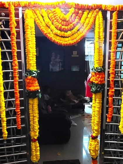 Marigold flower decorations for a steel gate at a housewarming. The bright yellow and orange garlands stand out against the metal gate.