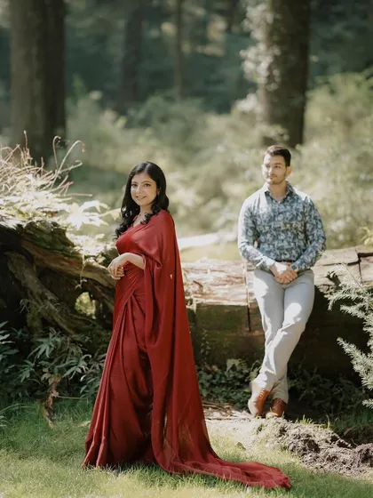 A pre-wedding shoot in a sun-dappled forest. The bride's flowing red gown stands out beautifully against the green, creating a vibrant and romantic portrait.