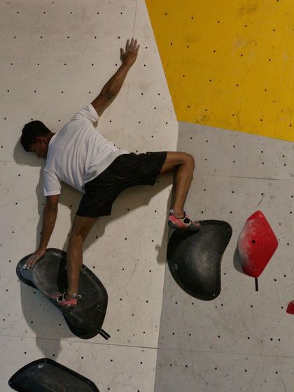 This photo captures the unique body positions and balance required for comp-style bouldering. This climber is using a large sloper hold to maintain balance.