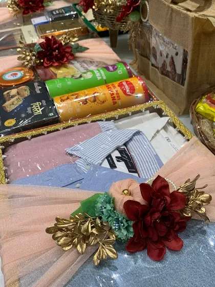 A close-up of a trousseau tray for the groom, featuring neatly folded shirts and a selection of snacks, all wrapped in clear film with a beautiful floral accent.