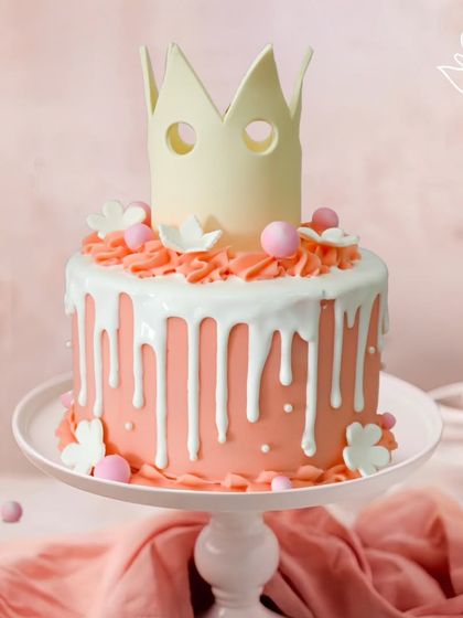 A stylish and modern princess cake, featuring a white chocolate crown on a pink drip cake. This design combines royal elegance with a trendy aesthetic for a unique celebration.
