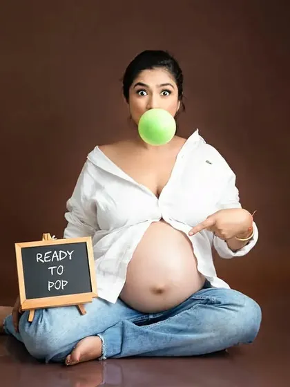 A fun and playful solo maternity shot featuring a "Ready to Pop" sign. This image showcases a more lighthearted and candid approach to pregnancy photography against a simple brown backdrop.