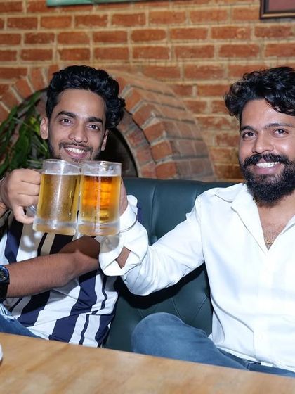 Two friends toasting with big mugs of beer. This is what it's all about, catching up with your buddies in a relaxed setting with good drinks and a lively background buzz.