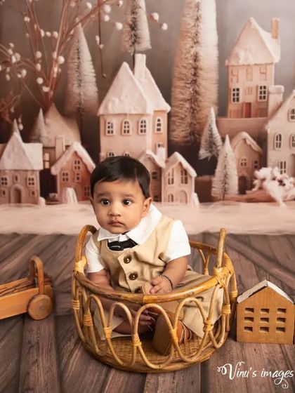 A cozy moment in a wicker basket. This portrait shows the baby sitting comfortably amidst the winter village scene, looking curiously at the camera.