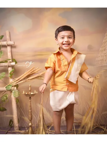 A joyful shot of the birthday boy in his traditional South Indian attire, surrounded by elements of a harvest theme.