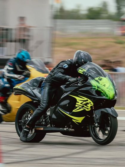 Two Suzuki Hayabusas, one black and one yellow, race side-by-side, creating a classic drag racing spectacle.