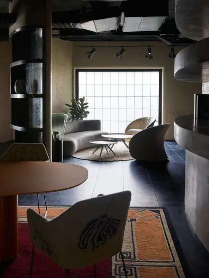 A moody and sophisticated seating area with a curved grey sofa and sculptural chairs. The large gridded window, although internal, mimics an external window, enhancing the 'mini-home' feel.