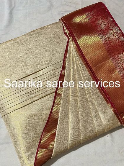 An off-white Kanjivaram saree with a red border. A classic choice for any auspicious occasion, now perfectly pleated.