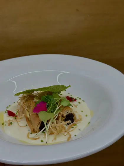 The third course, a beautifully plated Truffle Mushroom Éclair resting in a creamy parmesan sauce, garnished with microgreens and edible flowers.