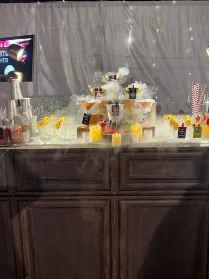 We love adding a bit of drama to our bar setups. This bar features an impressive display of cocktails enhanced with a theatrical dry ice smoke effect, creating an instant 'wow' factor for arriving guests.
