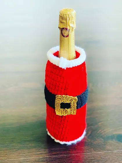 A classic Santa suit wine bottle cover, featuring his red suit, black belt, and gold buckle. It fits a standard wine or champagne bottle.