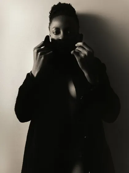 A moody and mysterious semi-nude portrait. The use of deep shadows and a large coat to obscure the body creates a sense of intimacy and intrigue.