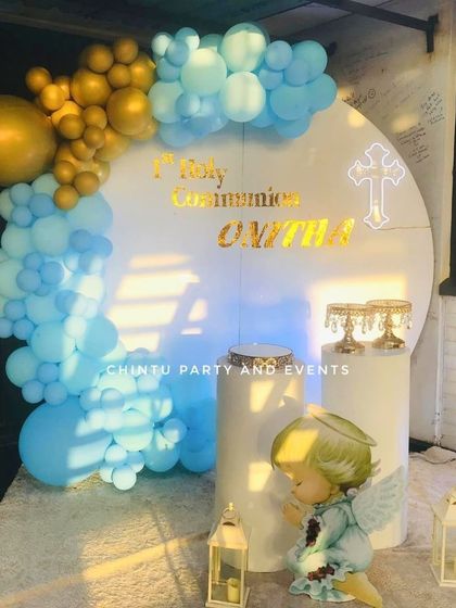 A First Holy Communion decoration for a girl with a praying angel prop. The blue, white, and gold balloon arch creates a heavenly feel.