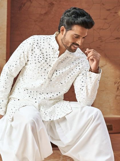 Shine bright this festive season. This all-white kurta is elevated with mirror-work embroidery and paired with flowing dhoti-style pants for a dramatic and celebratory look.