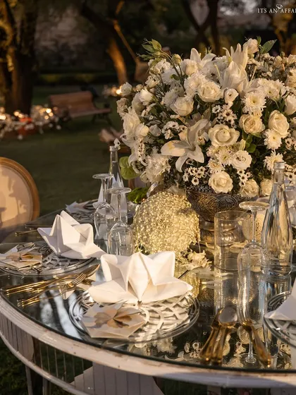 A detailed shot of the mirrored tabletop, reflecting the crisp white napkins, glassware, and abundant floral centerpiece.