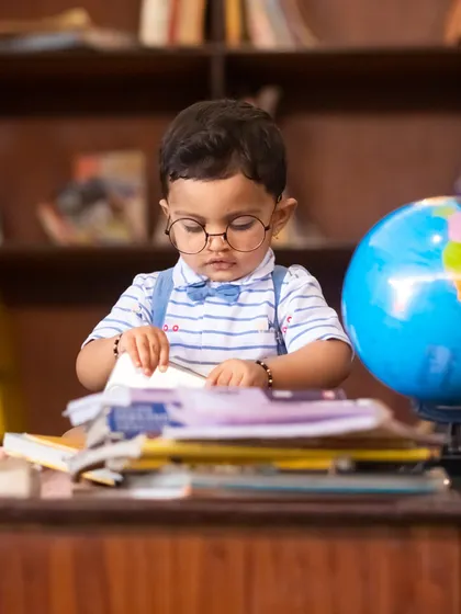 A studious-looking baby carefully turning the pages of a book during his library-themed milestone session.