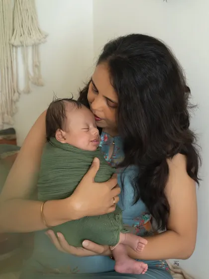The little one is smiling in their sleep. Capturing a newborn's fleeting smile while being cuddled by mom is a truly magical and rare moment.