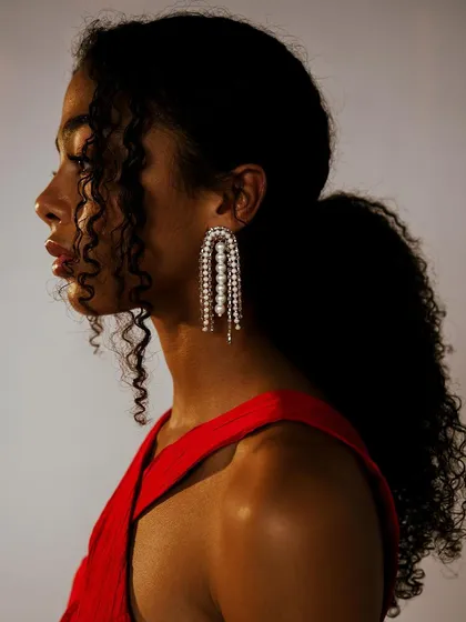 A classic profile shot for Melova, highlighting statement pearl earrings. The lighting is focused to accentuate the jewelry and the model's silhouette.