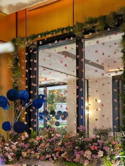 A window framed with a garland of greenery and hanging pastel flowers, with a pop of color from blue floral spheres. This shows how I frame existing views to incorporate them into the decor.