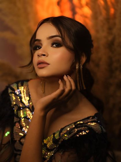 A classic glamour shot with a confident gaze and elegant hand gesture. The warm tones and soft background create a luxurious feel.