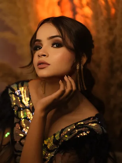 A classic glamour shot with a confident gaze and elegant hand gesture. The warm tones and soft background create a luxurious feel.