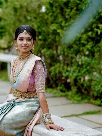 A bride seated on a bench, her pastel saree spread around her. This shot highlights the beautiful color combination and the intricate work on the blouse.
