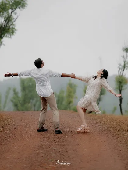 A fun, carefree moment with a couple holding hands and leaning back with arms outstretched on a country road.