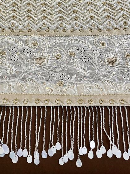 A close-up of the saree's pallu, featuring a dense chevron pattern and floral motifs, all highlighted with mirrorwork and finished with hand-sewn tassels.