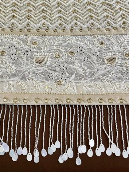 A close-up of the saree's pallu, featuring a dense chevron pattern and floral motifs, all highlighted with mirrorwork and finished with hand-sewn tassels.