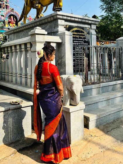 Our client Pooja radiates elegance in our signature blue and red designer silk saree, pictured here at a temple.