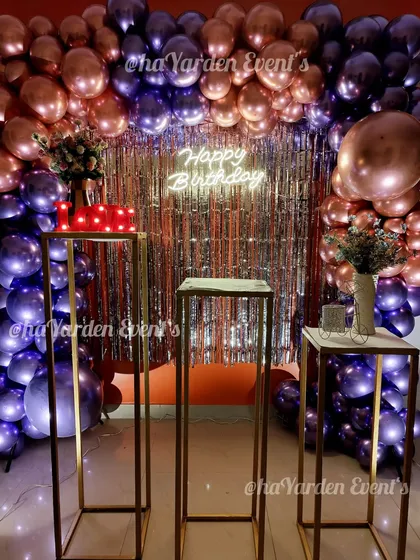 A dramatic and luxurious birthday setup with a wall of metallic purple and rose gold balloons. The silver fringe curtain and neon sign add extra layers of texture and light.