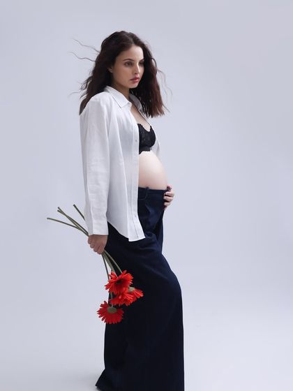 A striking and editorial-style portrait. The simple white shirt, dark trousers, and bold red flowers create a modern, artistic image that is both strong and feminine.