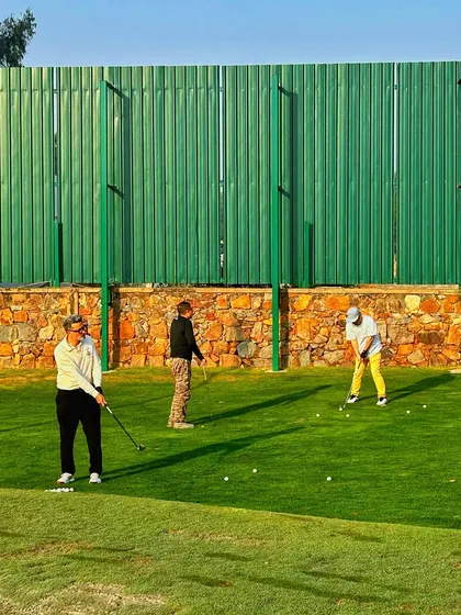 Three golfers practice their chipping and pitching near the stone wall boundary of our short game area.