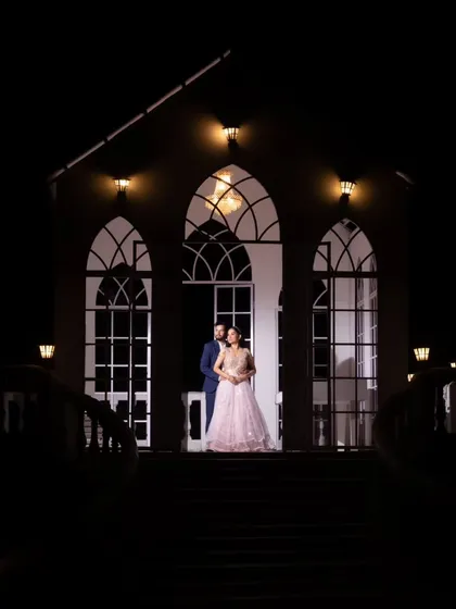 A dramatic night shot in front of a beautifully lit chapel-like structure. The color version highlights the bride's pastel gown against the dark, romantic setting.