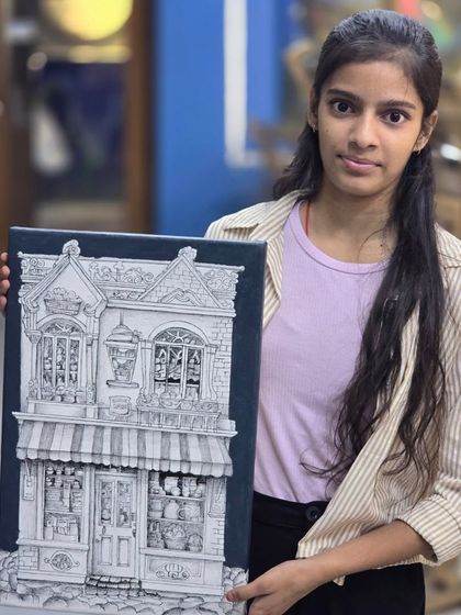 The student proudly holds her finished micron pen artwork, a beautiful and intricate piece that required hours of dedicated work.
