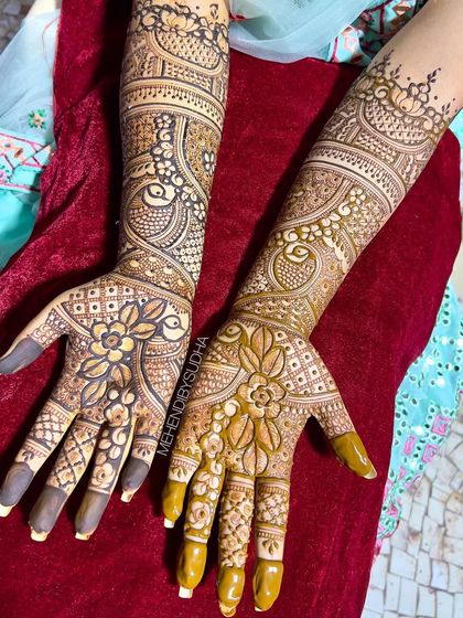A detailed view of the bride's mehendi, showing the combination of floral mandalas on the palms and peacock motifs on the arms.